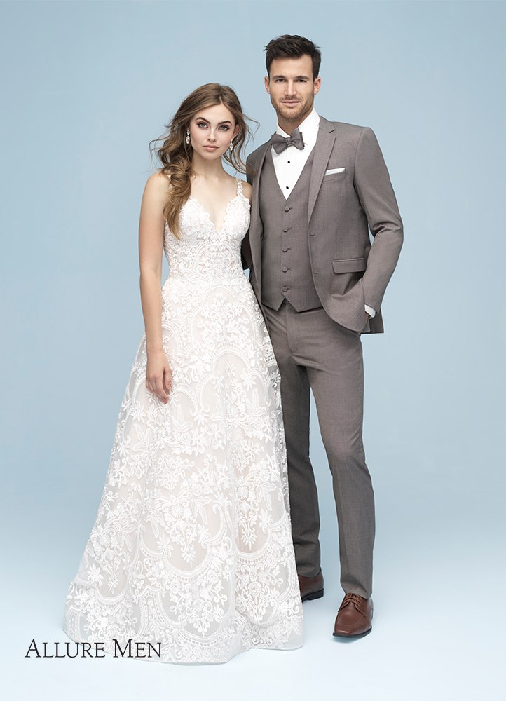 A handsome man in the Sandstone Beige Brunswick Suit by Allure Men stands next to his bride in a white wedding dress.