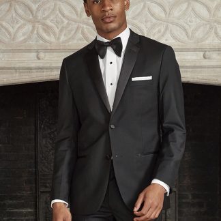 A Man in a black tuxedo stands in front of a fire place