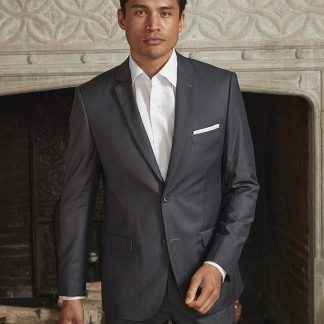 A man in a grey suit stands in front of a fireplace.