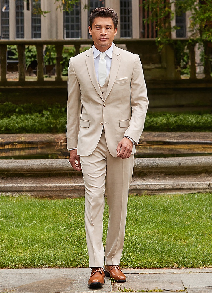 A Man in a Tan sharkskin power stretch suit walks towards the camera in front of a nice estate home