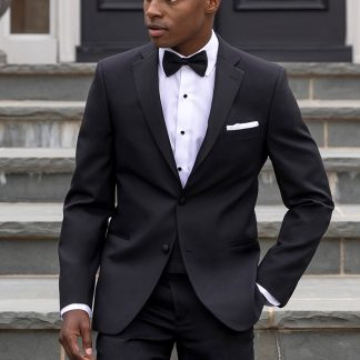 A handsome black man wearing the black 'Quincy' tuxedo walks down a flight of concrete stairs in front of a gorgeous mansion with his hand causally in one pocket.